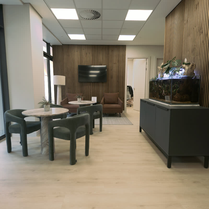Open waiting lounge with green chairs, marble tables and the planted aquarium on a dark sideboard