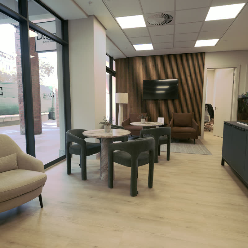 Waiting lounge with green boucle chairs and marble tables beside floor-to-ceiling shopfront windows