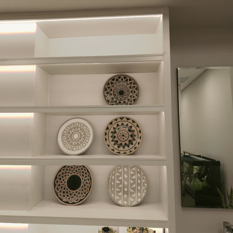 Hand-painted African ceramic plates with geometric patterns on warm backlit white shelving