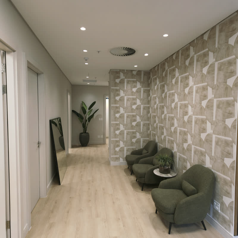 Olive-green armchairs beside a small side table against patterned wallpaper in a bright waiting nook