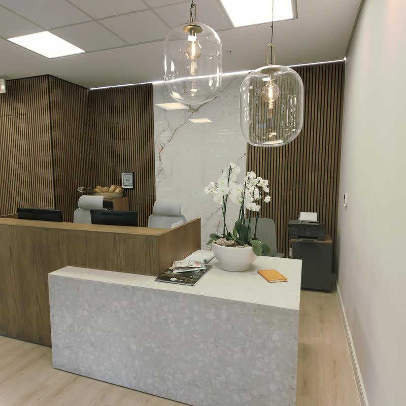 Reception desk with a white terrazzo counter, walnut slat walls, glass pendant lights and a white orchid