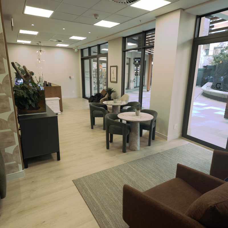 Sunlit waiting area with green upholstered chairs around stone tables, a planted aquarium and the timber reception desk