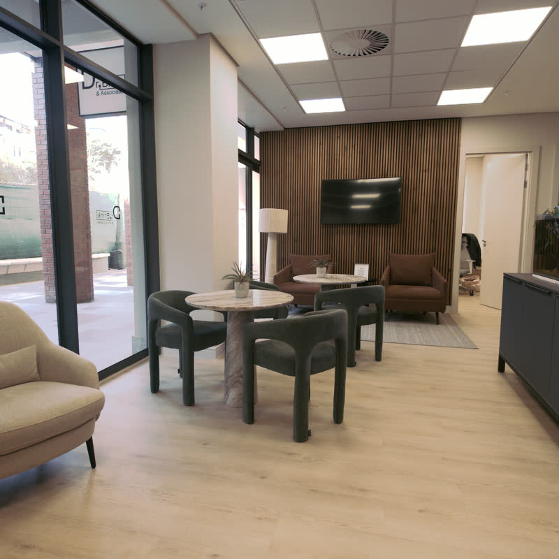 Waiting room with green boucle chairs, marble pedestal tables and floor-to-ceiling windows